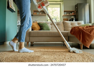 Woman is vacuuming floor of modern apartment living room, using portable cordless vacuum cleaner. Daily routine and household chores - Powered by Shutterstock