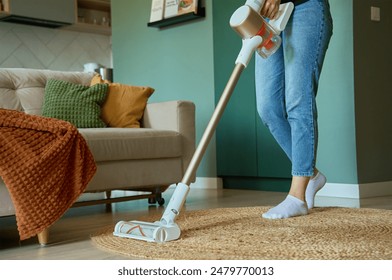 Woman is vacuuming floor of modern apartment living room, using portable cordless vacuum cleaner. Daily routine and household chores - Powered by Shutterstock