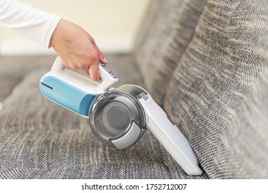 A woman vacuuming furniture in a house with a hand-held portable vacuum cleaner.