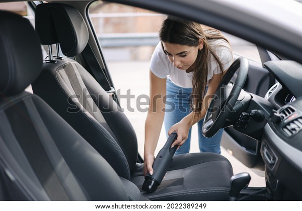 Woman vacuuming her car in the garage at home.\
Female using portable vacuum cleaner to remove dust and dirt. Car\
interior cleaning