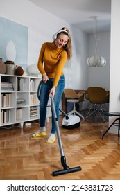 woman vacuuming at home and listening music - Shutterstock ID 2143831723