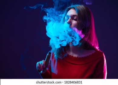 Woman Vaper Blows Smoke. Girl Uses A Vape Pen. Vape Pen In Girl Hand. Portrait Of A Smoking Woman On Dark Background. Use Of Electronic Cigarettes. Concept - Sale Of Vape Pen. Vaping Student