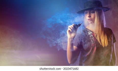 Woman vaper. Girl holds vape device. Stylish girl with electronic cigarette. Woman holds vape device. Woman vaper in clouds of smoke. Concept - smoking nicotine replacement. Alternative to cigarettes