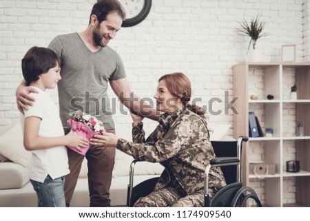 Woman Veteran In Wheelchair Homecoming Concept. Family Meeting. Son And Husband. Embrace With Mother. Camouflage Uniform. Child Hanging. Flowers Bouquet. Patriotic Comeback. Paralyzed Soldier.