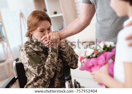 Woman veteran in wheelchair returned from army. The son and husband are happy to see her. Men give a woman in a wheelchair bouquet of flowers.