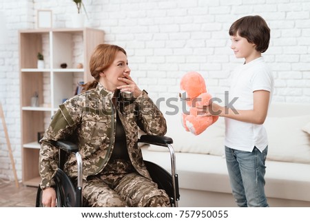 Woman veteran in wheelchair returned home. The son is happy to see his mother after returning from the army. The son gives his mother in a wheelchair a teddy bear.