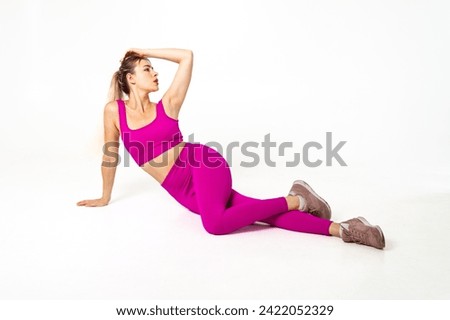Woman in vibrant pink sports outfit lying on floor with one hand on head