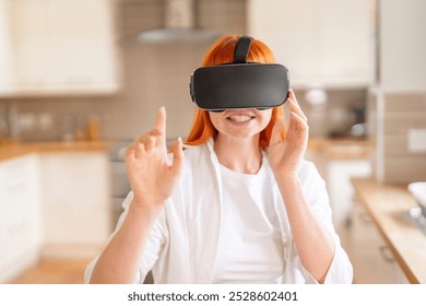 A woman with vibrant red hair enjoys virtual reality gaming in a cozy, modern kitchen - Powered by Shutterstock