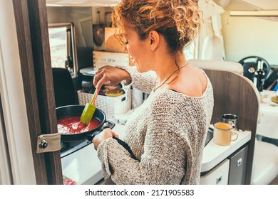 Woman Viewed From Back Preparing And Cooking Tomato Sauce For Lunch Inside A Modern Camper Van. Off Grid And Van Life Lifestyle With Traveler People Having Food Preparation. Indoor Kitchen Activity