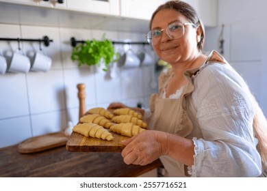 woman in vintage dress, apron preparing croissants, Unbaked, flaky croissants on wooden board, prepared for oven, homemade pastry in kitchen interior - Powered by Shutterstock