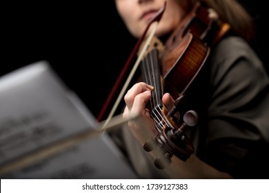 Woman violinist playing a classical baroque violin viewed past a music score on a stand with selective focus to her fingers on the strings