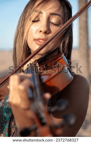 Woman violinist playing violin standing on the beach on the sand with the sea in the background. Close-up. Sunny afternoon