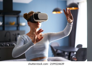 Woman in virtual reality goggles enters metaverse, controls immersive experience with hand gestures via headset interface in minimalistic interior. Girl gaming in cyber space. Futuristic concept. - Shutterstock ID 2199224639