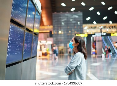 Woman in virus protection face mask looking at information board checking her flight in international airport. Departure board, flight status                             