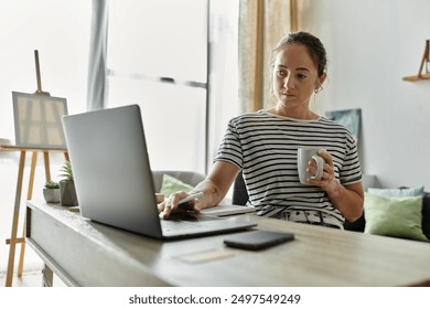 A woman with vitiligo sips coffee while working on her laptop.