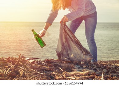 Woman Volunteer Helps Clean The Beach Of Trash. Earth Day And Environmental Improvement Concept. Ecology And Safety For Future Generation. Light From The Left Corner.