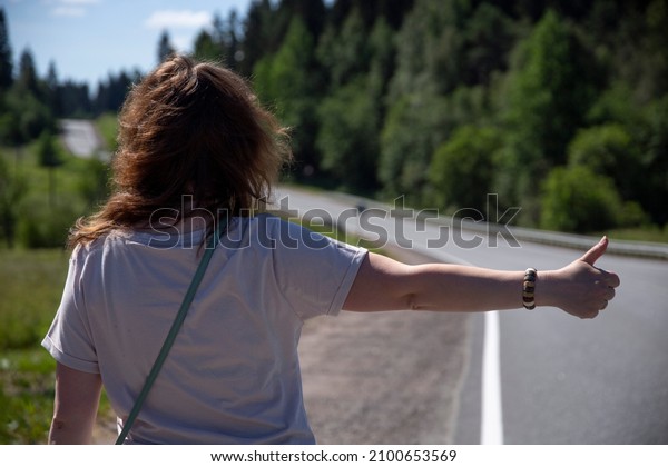 A woman votes with her hand to stop a car on\
a rural road. Hitchhiking.