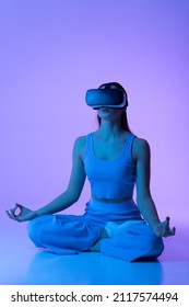 Woman In VR Glasses Sits In A Lotus Position. Engaged In Virtual Meditation. Yoga In Virtual Reality.