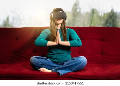 Woman In VR Glasses Sits In A Lotus Yoga Position Joining Hands - Virtual Meditation - Girl Taking Yoga Classes In Virtual Reality - Lifestyle And Technology Concept