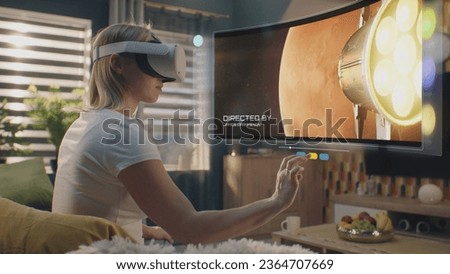 Woman in VR headset chooses movie or TV show to watch at home. 3D futuristic hologram shows interface of streaming service application and widgets in user menu. VFX animation. Concept of lifestyle.