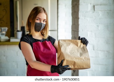 Woman Waiter In Protective Medical Mask And Gloves Work With Takeaway Orders. Waiter Giving Takeout Meal While City Covid 19 Lockdown, Coronavirus Shutdown. Paper Craft Bag With Food For Delivery