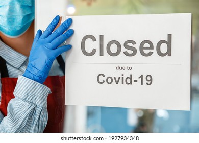 Woman Waiter In Protective Medical Mask Hangs Closed Sign On Front Door Of Cafe. Sign Closed Due To Covid 19 On Shop Entrance Door As New Normal Shutdown. Lockdown Coronavirus Covid.