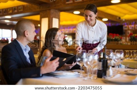 Woman waiter is taking order from clients in restaurante indoor