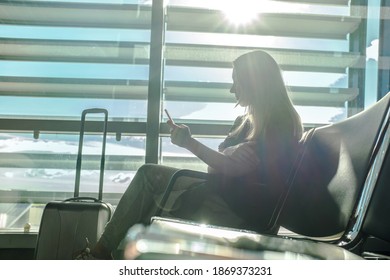 Woman waiting aircraft in airport. Young Female tourist traveling using her smartphone device. Online registration in mobile application.