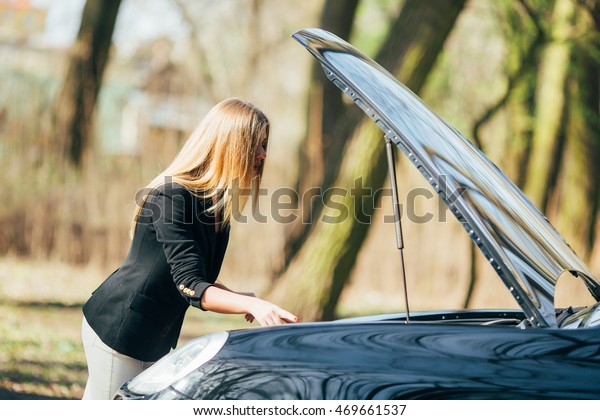 A woman waits for assistance near her car broken\
down on the road side.