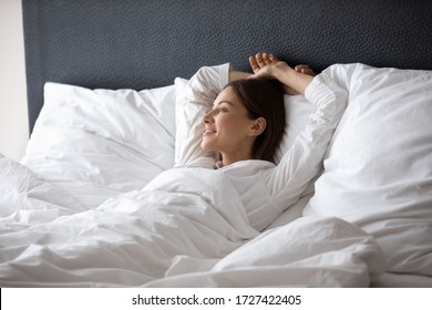 Woman wake up lying in bed dreaming planning day enjoy good morning vacation in hotel bedroom. Carefree 30s female relish comfy rest, warm duvet, put head behind head breath fresh air relaxing at home