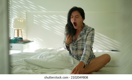 Woman waking up in the morning sitting in bed yawning. Person wake up