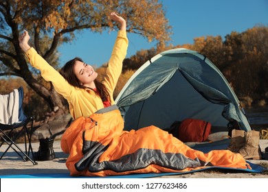 Woman Waking Up In Sleeping Bag Near Tent Outdoors