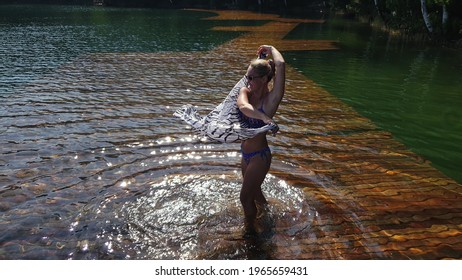 Woman walk on water on pier in sunglasses and a boho silk shawl. Girl rest on flood wood underwater dock. The pavement is covered with water in lake. - Powered by Shutterstock