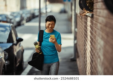 Woman walking after workout smiling and checking phone carrying water bottle and gym bag - Powered by Shutterstock