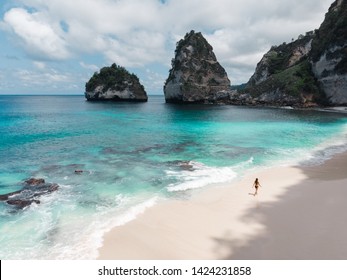 Woman walking alone on amazing tropical white sand beach. Aerial drone view from above. Tropical background and travel concept. Flying high above unrecognizable tourist girl exploring  tropical island