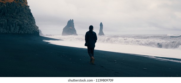 Woman walking alone on black sand beach at Reynisfjara, Iceland.  - Powered by Shutterstock