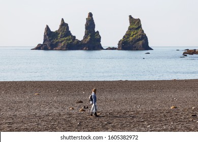 Woman Walking Along the Beach Looking at the Prominent Sea Stacks in Vik, Iceland - Powered by Shutterstock