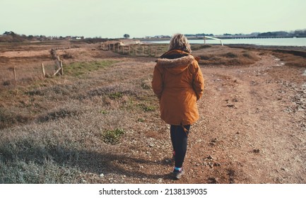 Woman walking along shoreline next to a river