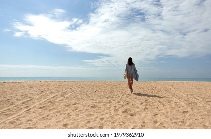 Woman walking away in the distance across a sandy tropical beach to the sea on a sunny spring or summer day with copy space in a vacation or travel concept - Powered by Shutterstock