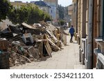 A woman walking away from a massive pile of destroyed, mud-covered discarded equipment and property after the devastating floods in Opava, September 21, 2024. Sunny, dusty, recovery, Czechia, cleaning