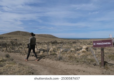 A woman walking away from a sign stating Pinguinera Penguin colony at Monte Leon National Park - Powered by Shutterstock