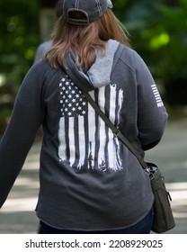 A Woman Walking Away Wears A Grey Hooded Sweatshirt With An American Flag On Its Back