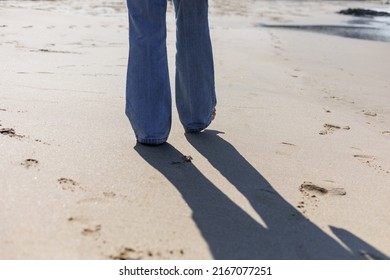 Woman Walking Barefoot On The Beach In Blue Jeans 