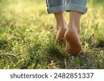 Woman walking barefoot on green grass outdoors, closeup. Space for text