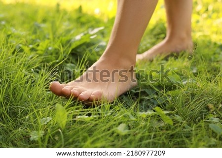 Woman walking barefoot on green grass, closeup