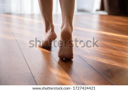 Woman walking barefoot on toes at warm laminate floor close up rear view. Sunny light bedroom good morning welcome new day, modern comfy apartments with under floor heating system, footcare concept