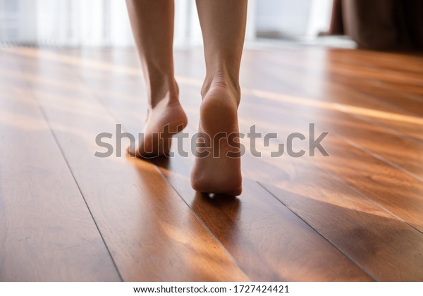 Woman walking barefoot on toes at warm laminate\
floor close up rear view. Sunny light bedroom good morning welcome\
new day, modern comfy apartments with under floor heating system,\
footcare concept