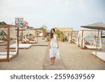 Woman Walking Barefoot on Wooden Pathway in Beach Resort with Elegant Cabanas 