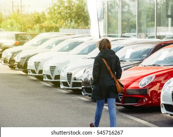 Woman walking between rows of new car to choose the most precious one at the Alfa Romeo car store