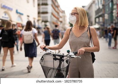 Woman walking by her bicycle on pedestrian city street wearing medical face mask in public to prevent spreading of corona virus. New normal during covid epidemic. Social responsibility. - Powered by Shutterstock